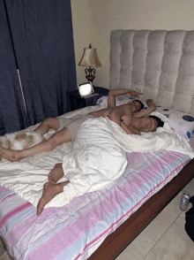 two men are laying on a bed with a lamp on the nightstand