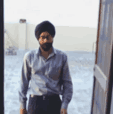 a man wearing a turban and glasses stands in front of a door