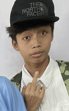 a young man wearing a black north face hat giving the middle finger