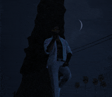 a man in a white shirt and tie is standing in front of a tree at night