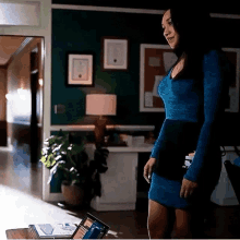 a woman in a blue dress is standing in a room next to a laptop computer .