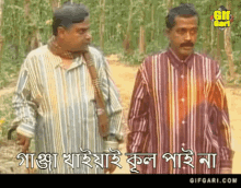 two men in striped shirts are standing next to each other on a dirt road with trees in the background .