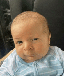 a baby is wearing a blue and white striped outfit and making a funny face