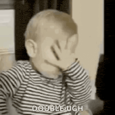 a baby is covering his face with his hand while wearing a striped shirt .