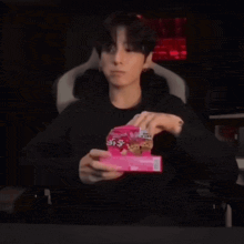 a young man is sitting in a chair holding a box of cookies in his hands .