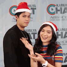 a man and a woman wearing santa hats are posing for a picture in front of a wall that says kapamilya