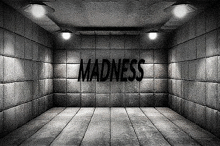 a black and white photo of a room with a brick wall and the word madness written on it .