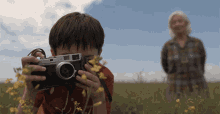 a young boy is taking a picture of a woman in a field with tales from the loop written above him