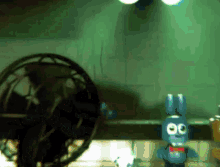 a toy bunny is standing next to a fan in a dark room