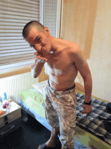 a shirtless man is standing in front of a bed and giving the peace sign