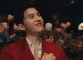 a young man in a red jacket is smiling in front of a bunch of flowers .