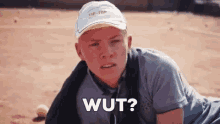 a young man wearing a hat and a gray shirt is laying on a tennis court and saying wut .