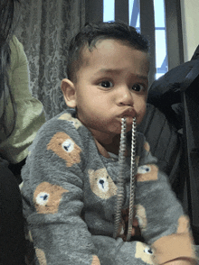 a baby wearing a teddy bear outfit is holding a pencil in its mouth