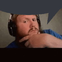 a man with a beard wearing headphones and a blue shirt is looking at the camera .