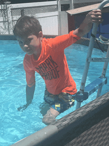 a boy in an orange shirt that says shark proof is standing in a pool