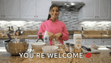 a woman in a pink chef 's coat is preparing food in a kitchen and the words you 're welcome are above her