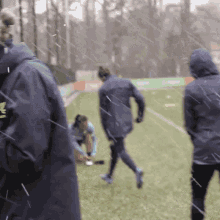 a group of people standing on a field in the rain with one wearing a jacket that says adidas on it