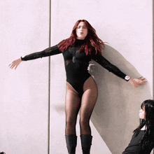 a woman with red hair is wearing a black leotard and tights