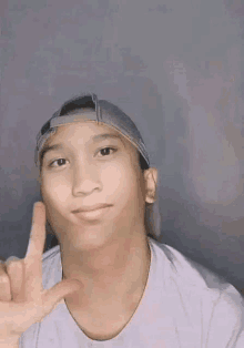 a young man wearing a hat and a white shirt is making a funny face and giving a peace sign .