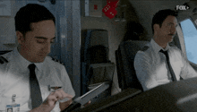 two pilots are sitting in the cockpit of an airplane and one is looking at his tablet