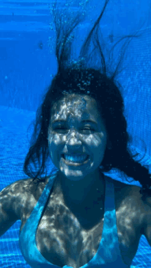 a woman in a blue bikini is swimming underwater and smiling