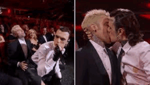 a couple of men in suits are kissing in front of a crowd of people .