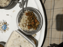 a bowl of rice with peas and carrots sits on a table next to a container of yogurt