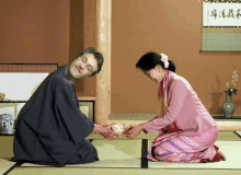 a man in a kimono is kneeling down and giving something to a woman