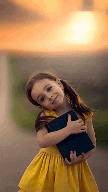 a little girl in a yellow dress is holding a bible in her hands