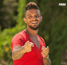 a man in a red shirt is pointing at the camera with the letters prbk on the bottom right