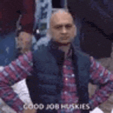 a man in a plaid shirt and vest is standing with his hands on his hips and says `` good job huskies '' .