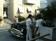 a group of people are standing in front of a black car with a license plate that says ' aa ' on it