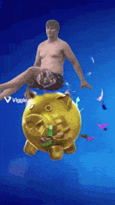 a shirtless man is sitting on top of a gold piggy bank that says viggles