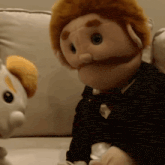 a puppet is sitting on a couch next to a stuffed animal