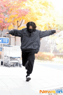 a person wearing a black nike jacket and black pants is running with their arms outstretched