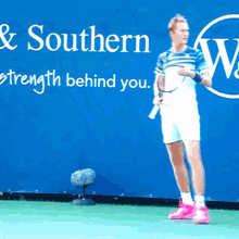 a man holding a tennis racquet stands in front of a sign that says " & southern strength behind you "