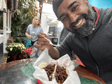 a man with a beard is eating a taco with a woman in the background