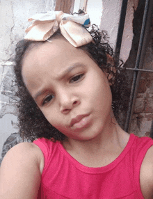 a little girl with curly hair wearing a pink tank top and a bow in her hair