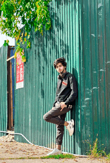 a young man leaning against a green wall wearing headphones and a sweatshirt that says tr