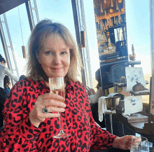 a woman in a red leopard print shirt holds a glass of champagne