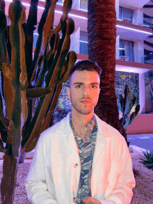 a young man in a white jacket stands in front of a cactus