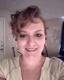 a woman wearing earrings and a white shirt smiles for the camera