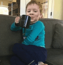 a young boy is sitting on a couch holding a cup