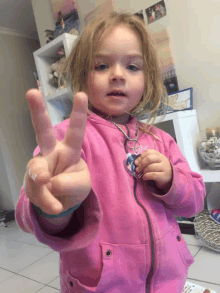 a little girl in a pink jacket is making a peace sign with her fingers