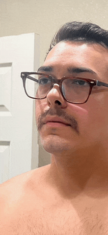 a man with glasses and a mustache is looking at himself in a mirror