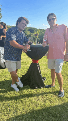 two men standing next to each other holding wine glasses in front of a table