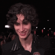 a young man with curly hair is smiling while wearing a black shirt and a yellow microphone with the letter t on it