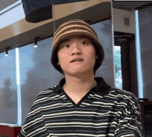 a man wearing a striped shirt and a beanie looks at the camera