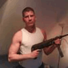 a man in a white tank top is holding a gun in a room .