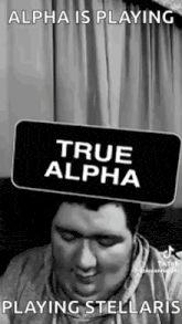 a man is sitting on a couch holding a sign that says `` true alpha '' .